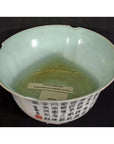 Pale green porcelain bowl with black script and two labels inside, on a black background.
