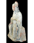 Terracotta Ming Dynasty seated court figure statuette in robes with hands on lap, close-up against black background.