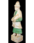 Close-up of a Chinese Ming Dynasty ceramic figure in green and cream robes with hat, on a black background.