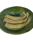 Green ceramic Ming Dynasty plate with four brown, spotted, banana-like objects, close-up view.