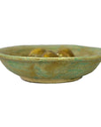 Rustic green ceramic Chinese Ming Dynasty plate with three small brown objects on a white background.