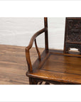 Close-up of a brown elmwood Chinese Ming Dynasty chair on a wooden floor with a white brick wall background.