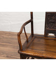 Close-up of a brown elmwood Chinese Ming Dynasty chair on a wooden floor with a white brick wall background.