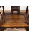 Brown elmwood Ming Dynasty chair with curved arms, carved backrest, visible wood grain on wooden floor indoors.