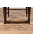 Close-up of light brown elmwood chair legs and stretcher on a light wood floor.