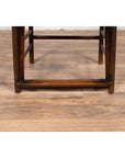 Close-up of light brown elmwood chair legs and stretcher on a light wood floor.