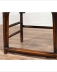 Close-up of brown elmwood Chinese Ming Dynasty chair, on light wood floor with white brick wall background.