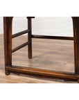 Close-up of brown elmwood Chinese Ming Dynasty chair, on light wood floor with white brick wall background.