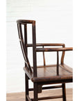 Brown elmwood Chinese Ming Dynasty chair with square backrest, side view, against white brick wall and wood floor.