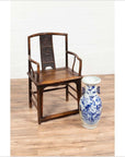 Brown elmwood Ming Dynasty chair beside white porcelain vase on wooden floor, indoors.