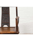 Close-up of brown elmwood Chinese Ming Dynasty chair, set indoors against a white brick wall.