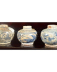 Close-up of three blue and white Chinese Ming Dynasty Swatow Ware ceramic jars on a dark wooden surface.