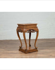 Dark wood Ming style incense stand with cabriole legs and carved apron, indoors against a white brick wall.