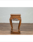 Dark wood incense stand with carved apron and cabriole legs on a wood floor against a white brick wall indoors.