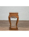 Dark wood incense stand with carved apron and cabriole legs on a wood floor against a white brick wall indoors.