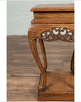 Close-up of a brown wooden Ming style incense stand with cabriole legs and carved apron, on a wood floor indoors.