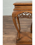 Close-up of a brown wooden Ming style incense stand with cabriole legs and carved apron, on a wood floor indoors.