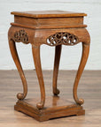Brown wooden incense stand with cabriole legs and carved apron, placed on a wooden floor by a white brick wall indoors.