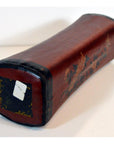 Close-up of antique Chinese leather opium pillow with black ends and floral design, on white surface with price sticker.
