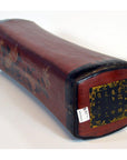 Red lacquered leather opium pillow with curved rectangular shape, floral designs, and Chinese characters on one end.