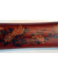 Brown lacquered wood opium pillow with yellow, orange, and green painted floral design, leather accents, close-up.