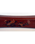 Red lacquer leather opium pillow with black ends and yellow-green floral designs, antique Chinese style, close-up view.