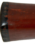 Close-up of reddish-brown antique opium pillow with worn edges next to a wooden didgeridoo.