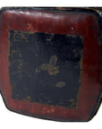 Close-up of antique opium pillow in worn dark red leather with a faded black square and faint central emblem.