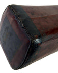 Close-up of a rectangular dark brown leather opium pillow with worn edges and visible stitching.