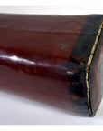 Close-up of a glossy red wooden rectangular opium pillow with black-edged end, shown against a plain background.