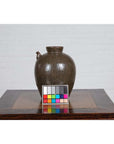 Green glazed ceramic water jug with petite spout on wooden table, white brick wall background, Qing Dynasty, 19th century.