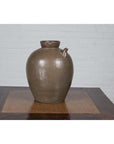 Glazed ceramic water jug with petite spout, 19th-c. Chinese Qing Dynasty, on wooden table by white brick wall.