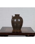 Glazed ceramic water jug with petite spout, 19th-century Qing Dynasty, on wooden table against white brick wall.