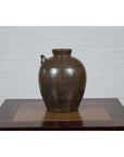 Green glazed ceramic water jug with petite spout, Qing Dynasty style, on wooden table by white brick wall.