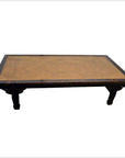 Light brown rattan coffee table, rectangular with woven top and four short carved legs, studio background.