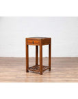 Brown elmwood lamp table with single drawer and cracked ice shelf on wooden floor next to white brick wall.