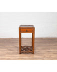 Brown elmwood lamp table with single drawer and cracked ice shelf on wood floor against a white wall indoors.