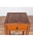 Brown elmwood lamp table with single drawer and cracked ice shelf on a wooden floor indoors.