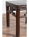 Close-up of dark wood Chinese side table leg with carved medallions on a wood-patterned floor.