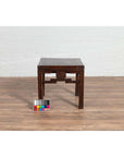 Dark wood Qing style side table with carved medallions, on wood floor next to white brick wall indoors.