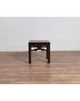 Dark wood Chinese side table with carved medallions, vintage Qing style, on wood floor by white brick wall indoors.