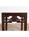 Dark wood Qing style side table with carved medallions, on wood floor against white brick wall.