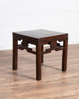 Dark wood side table with carved medallions, vintage Qing style, on wooden floor against a white wall indoors.