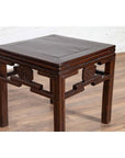 Dark wood Chinese Qing-style side table with carved medallions on light wood floor against white wall indoors.