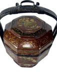 Close-up of brown lacquered octagonal Chinese wedding basket with gilt designs, black handle, and painted lid scene.