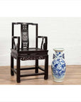 Dark wood Chinese wedding chair with curved pierced splat, serpentine arms, next to blue and white ceramic vase on wood floor.