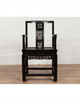 Dark wood Chinese Wedding Chair with curvy pierced splat and serpentine arms on wooden floor by white brick wall.