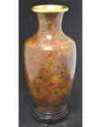 Red, gold, and brown cloisonné vase with floral patterns on a dark wooden stand, close-up view.