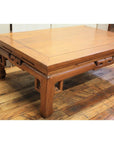 Brown wood coffee table with openwork aprons and carved geometric legs on a hardwood floor.