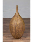 Mustard ceramic vase with tapered spout on wooden floor against white brick wall.